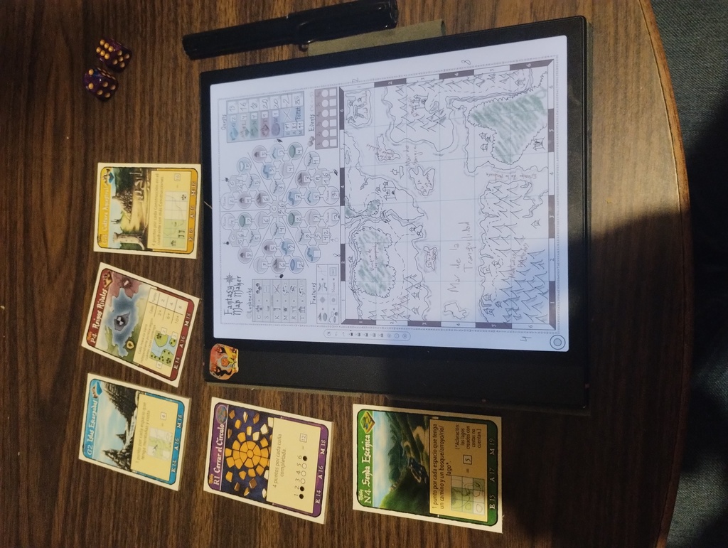 Foto de juego terminado, se ven las cinco cartas de misión, dos dados de seis caras, y una tablet con la hoja de juego